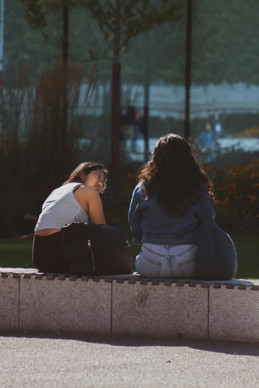two girls sitting on a wall, one looking at the other