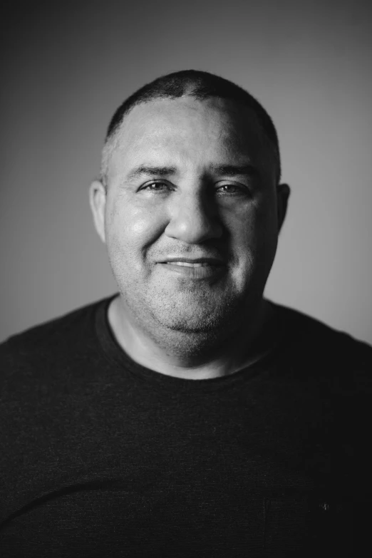 man smiling at camera against gray wall with one eye on the other