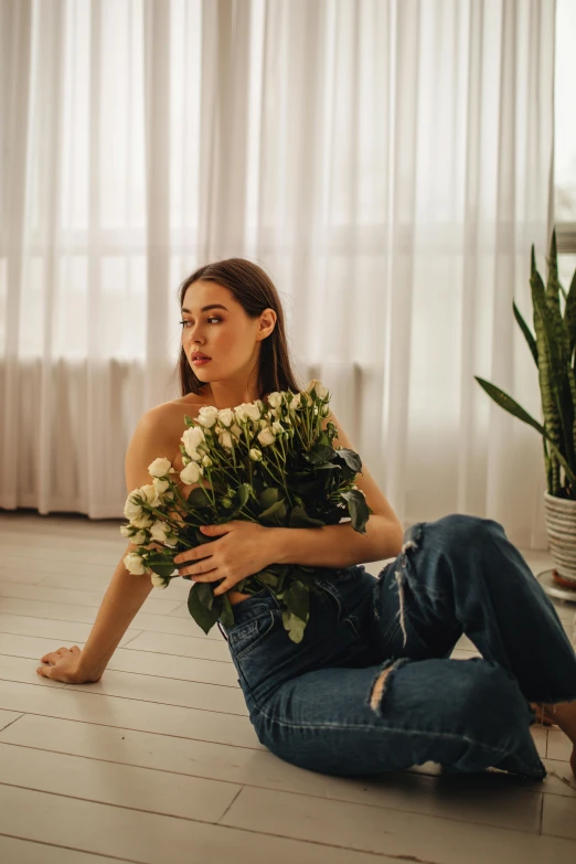 a woman with long hair sitting on the floor holding some flowers