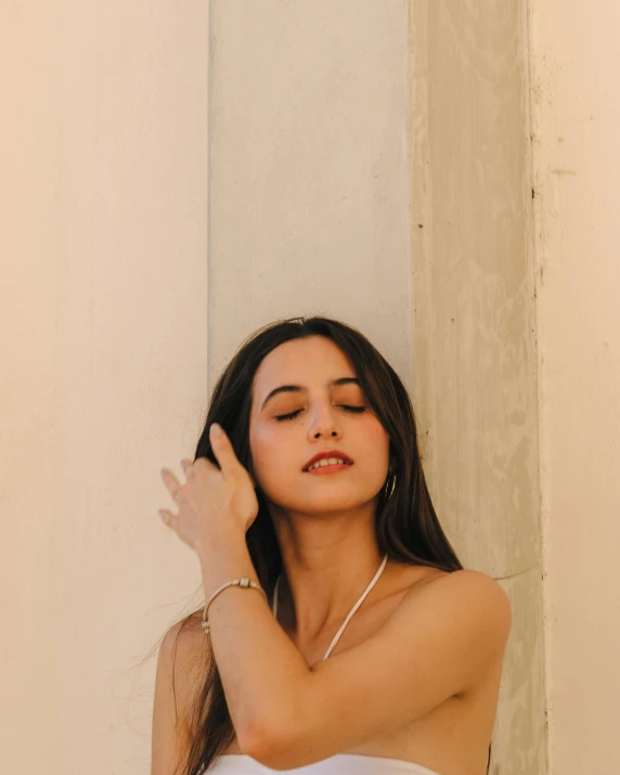 a woman standing next to a wall with her arm over her ear