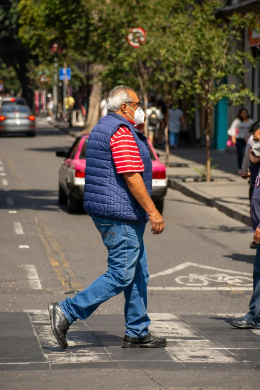 man with mask crossing the street on the sidewalk