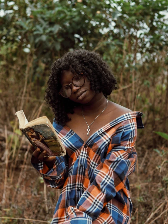 a woman standing and reading a book in front of bushes