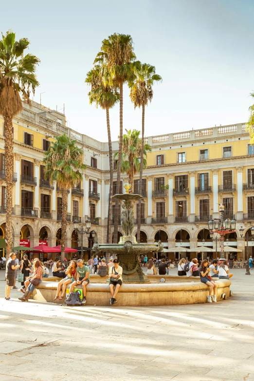 a large city square with benches, people, and tall palm trees
