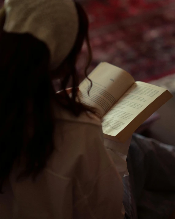 woman in brown jacket holding up open book on rug