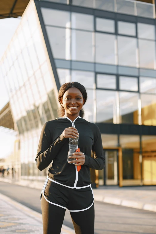 a woman wearing black running gear and carrying an orange water bottle