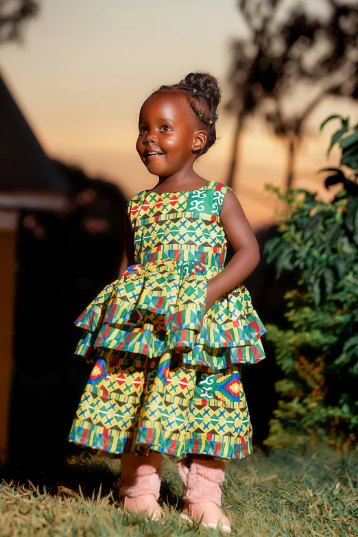 a little girl in a dress smiling and standing on the grass