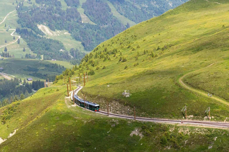 a long train coming down a track on top of a green hillside