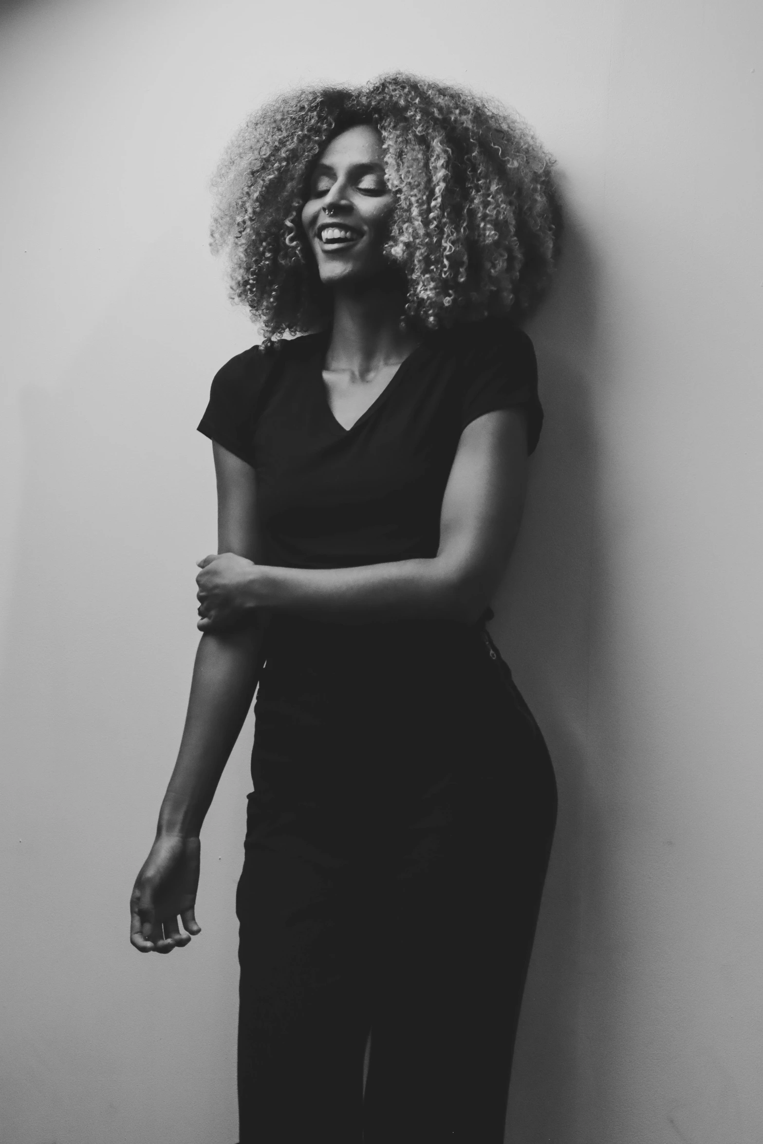 a smiling woman in a black and white po leaning against a wall