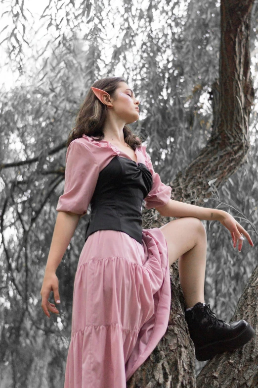 woman in pink dress sitting up on top of a tree