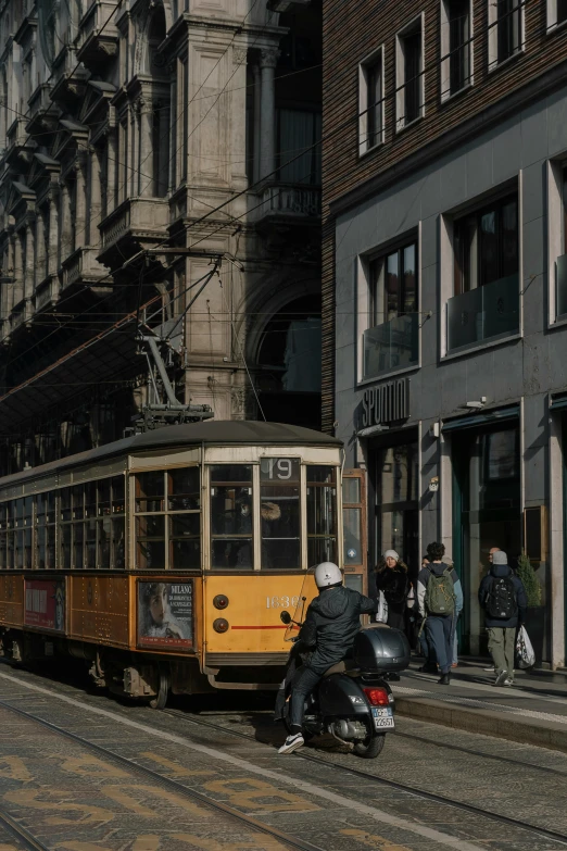 a person in black riding a motorcycle next to an orange trolley