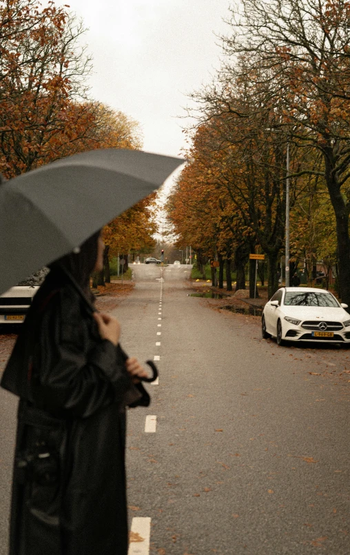 a woman holding an umbrella walks down the road