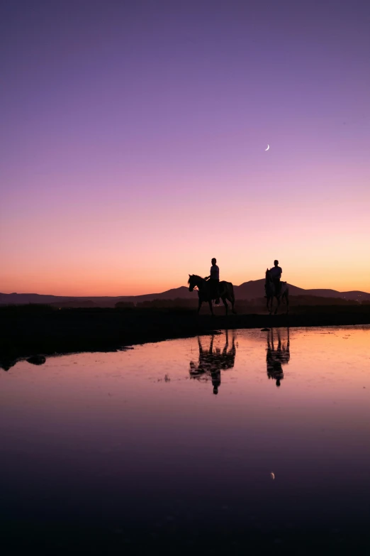 two people ride their horses by the water