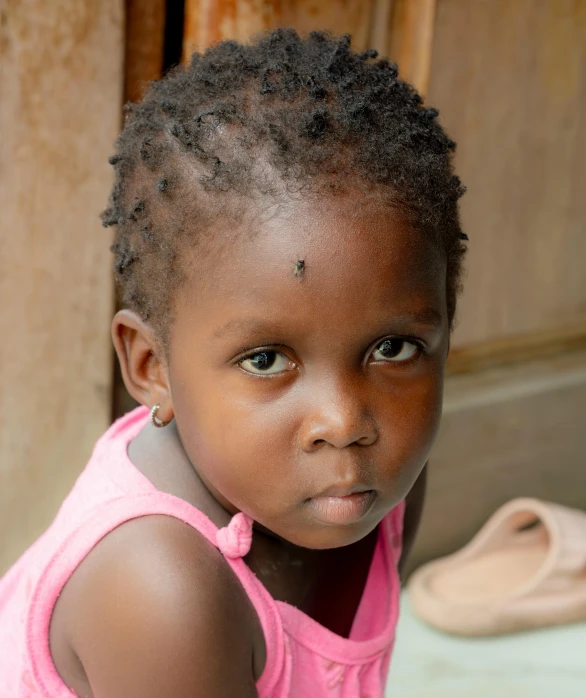 a young child wearing pink shirt sitting next to a wall