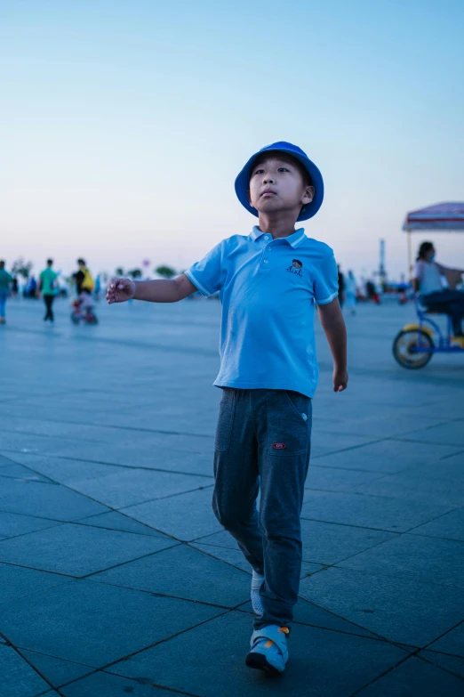 boy in hat is watching and smiling from the top of a cement sidewalk