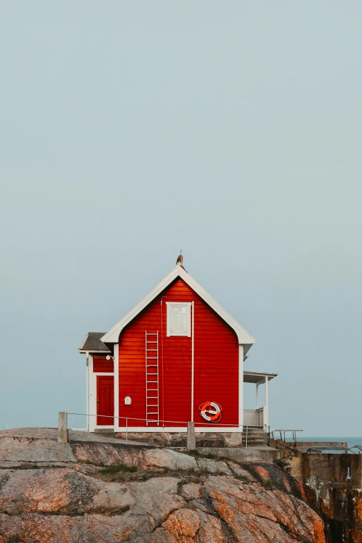 a red building on a rocky cliff with a ladder to it