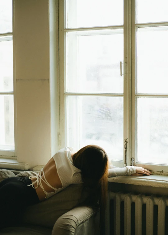 a young woman laying on the couch looking out of a window