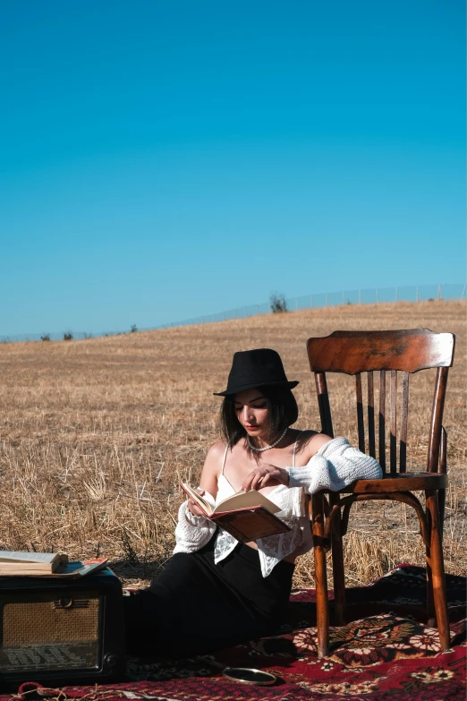 a woman in a hat sitting on a chair looking at a book