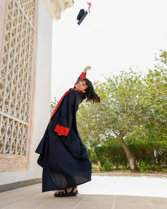 a woman in a graduation gown and cap throwing a kite