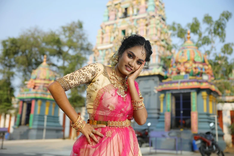 a woman posing in a colorful indian saree in front of a small temple