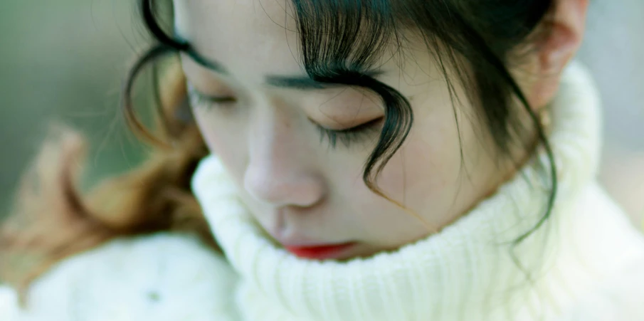 young lady with dark hair looking down wearing a turtle neck sweater