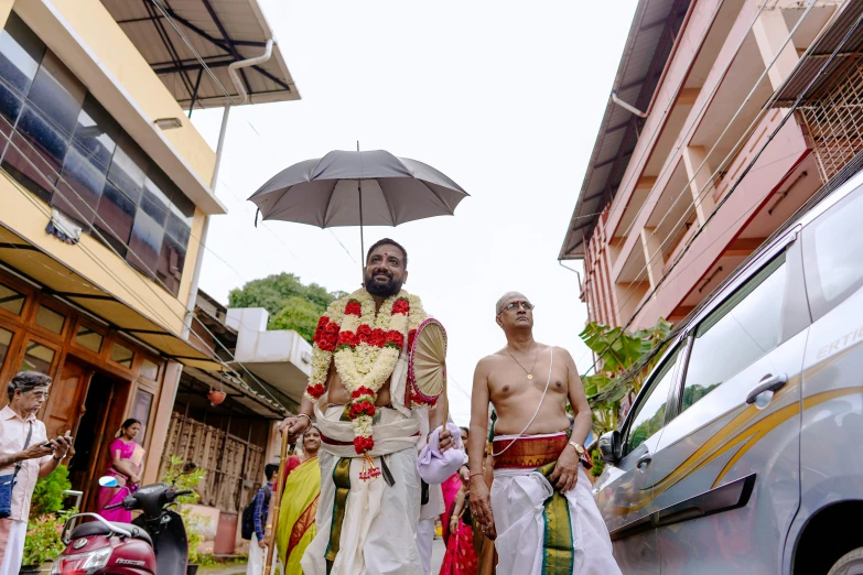 a man in white with a flower lei and a man with an umbrella walking down a street