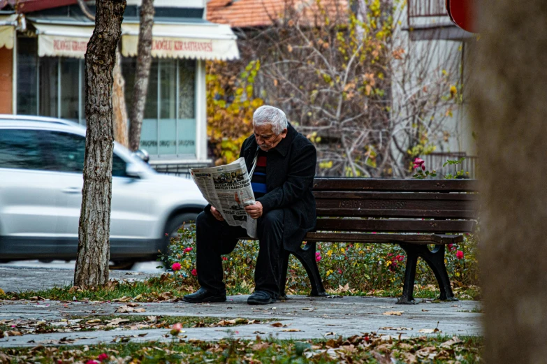 an old man sits on a bench reading a newspaper