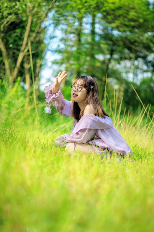 a girl sitting in the grass waving at soing