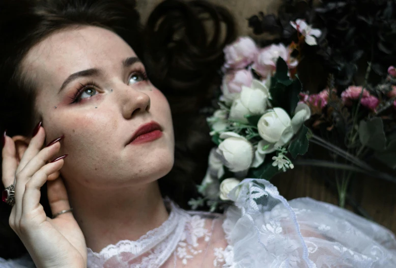 a woman in white sitting next to a bunch of flowers