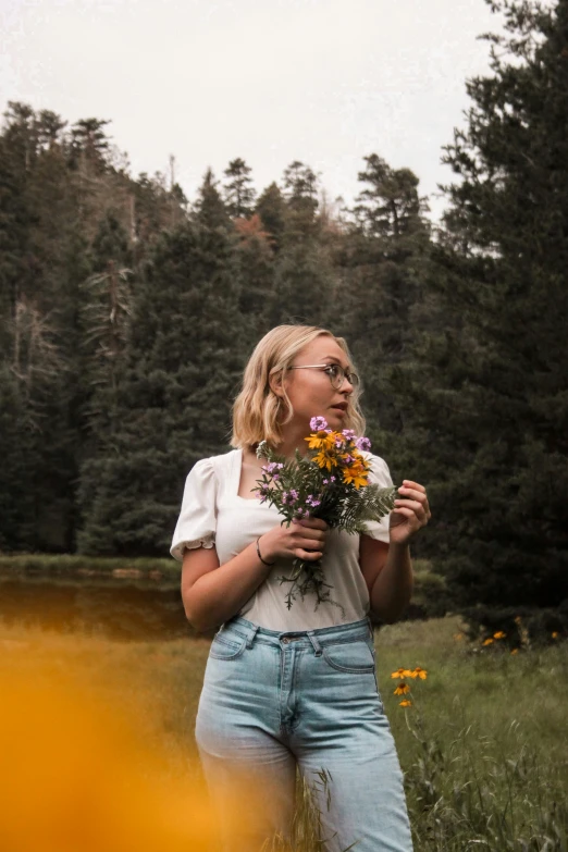 a blonde female in glasses stands outdoors with flowers