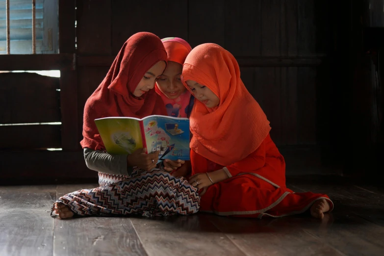 two women in orange clothing reading a book