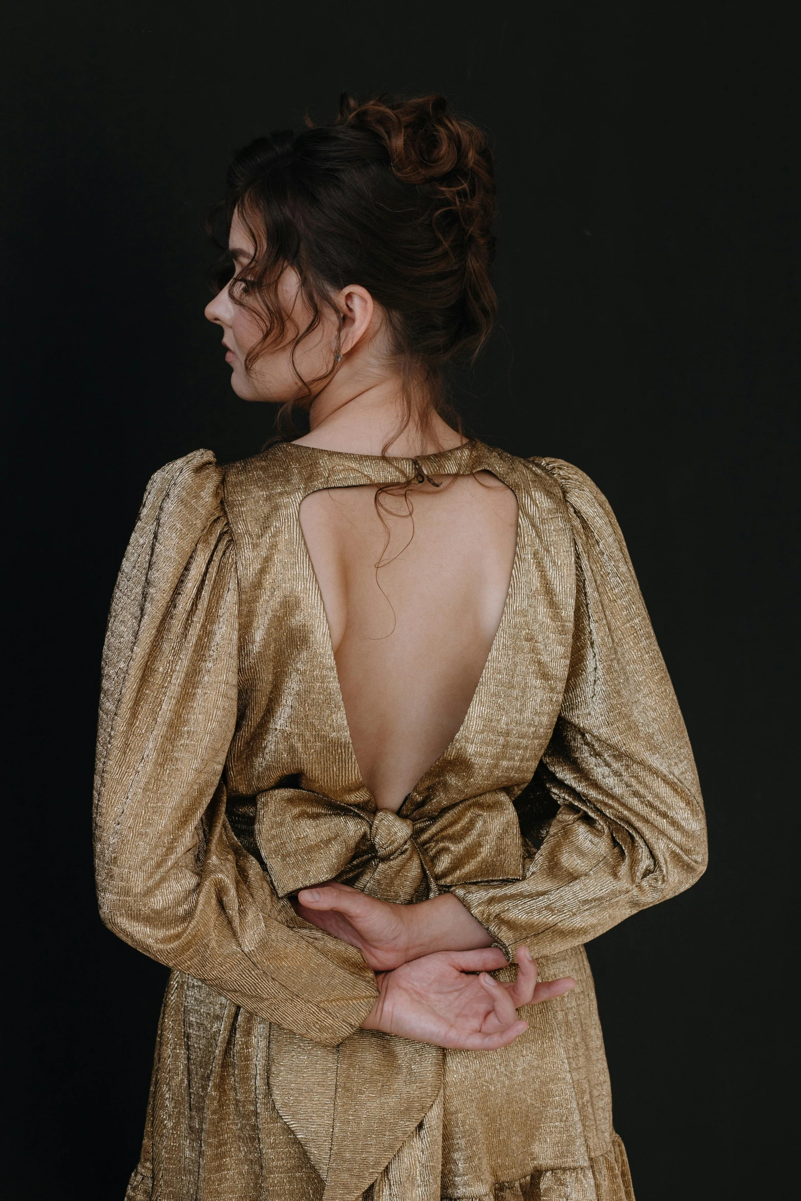 a woman in a gold dress stands against a black background