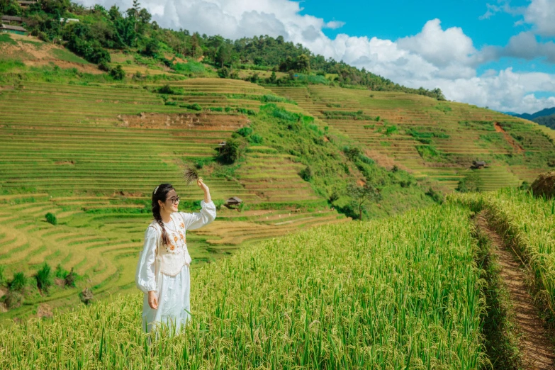 woman in white dress standing in field reaching up with finger