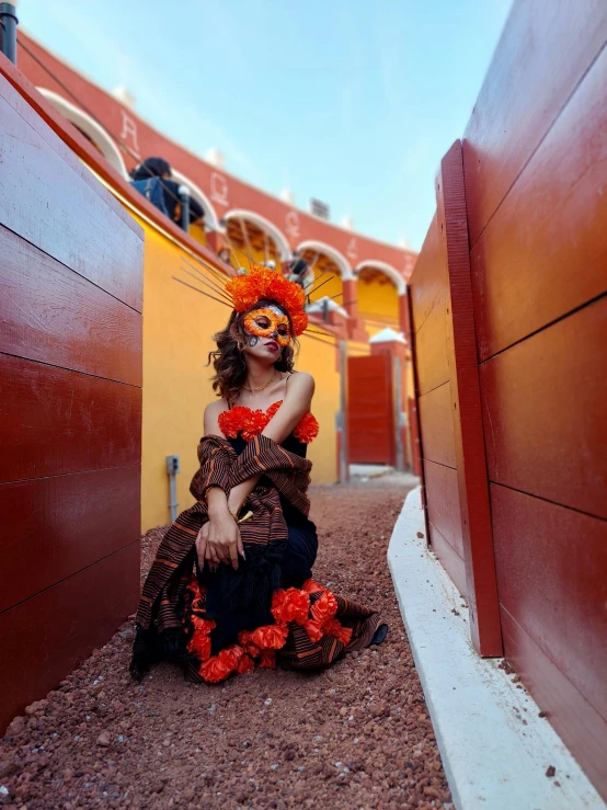 a woman dressed up like a carnival girl, seated in front of some red walls