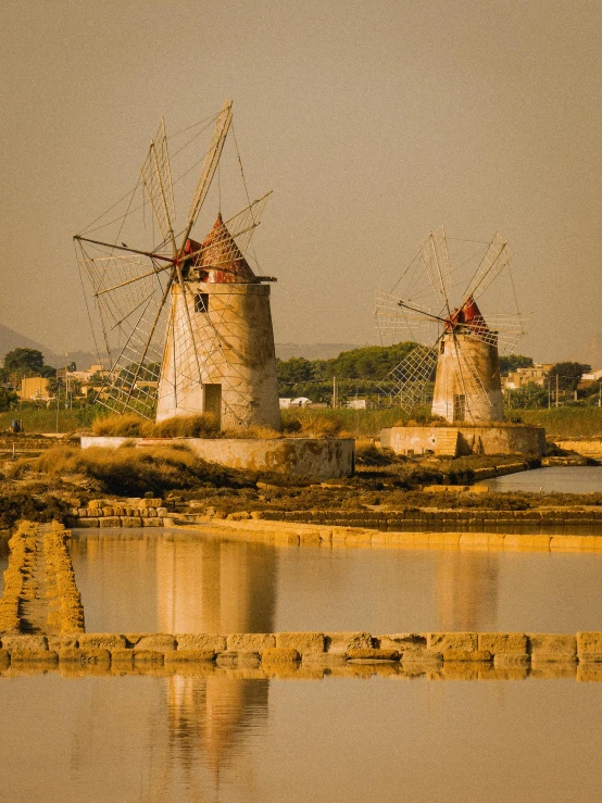 two windmills stand near the water as it reflects in the water