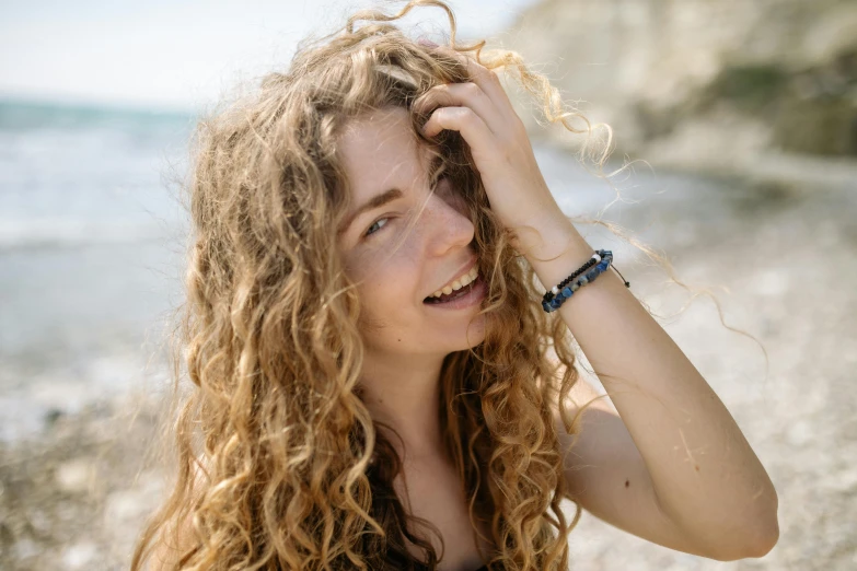 a woman holding her hair and looking at the beach