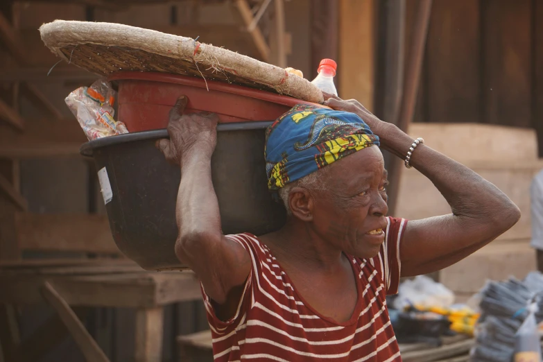 a woman carrying a bundle on her head in an area with other people in the background