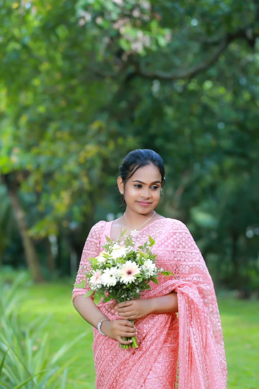 a lady wearing a pink and white saree and holding a bouquet