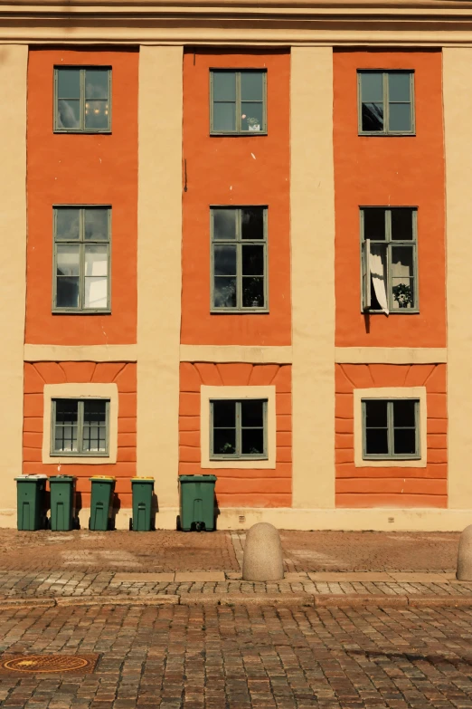 large orange building on the street with trash bins in front