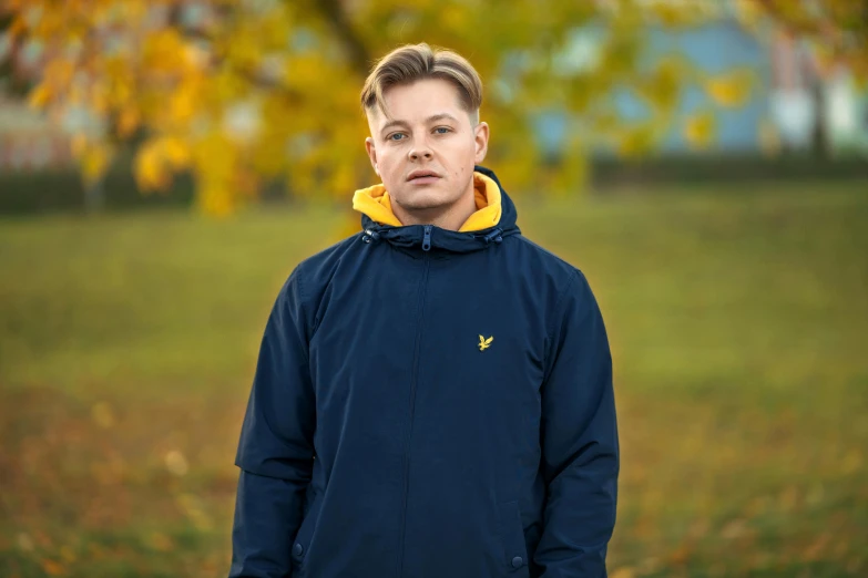 a  in blue coat standing under yellow autumn leaves