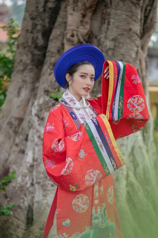 the woman in a traditional chinese outfit stands near a tree