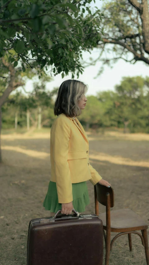 a woman in a yellow dress standing with a brown suitcase