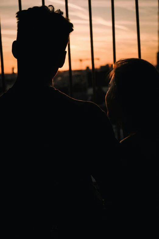 two people standing in front of some fence at sunset