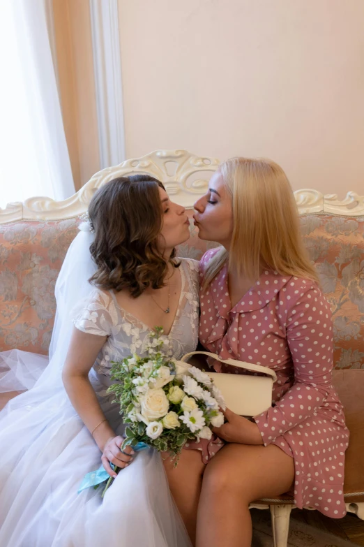 two ladies in dress sitting on a couch kissing