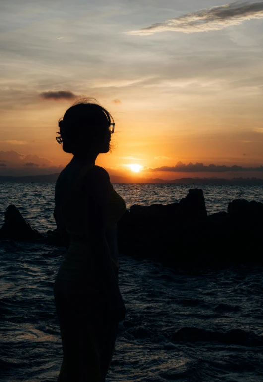 there is a woman standing in front of the ocean at sunset