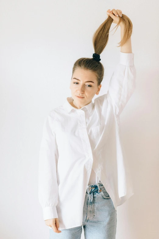 a woman in jeans and a shirt holding her hair up to her head