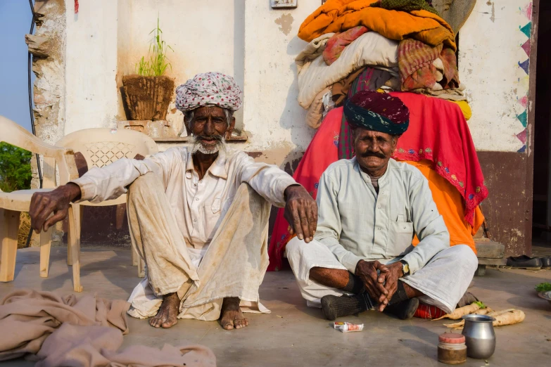 two men sitting outside a building with their hands on his knees