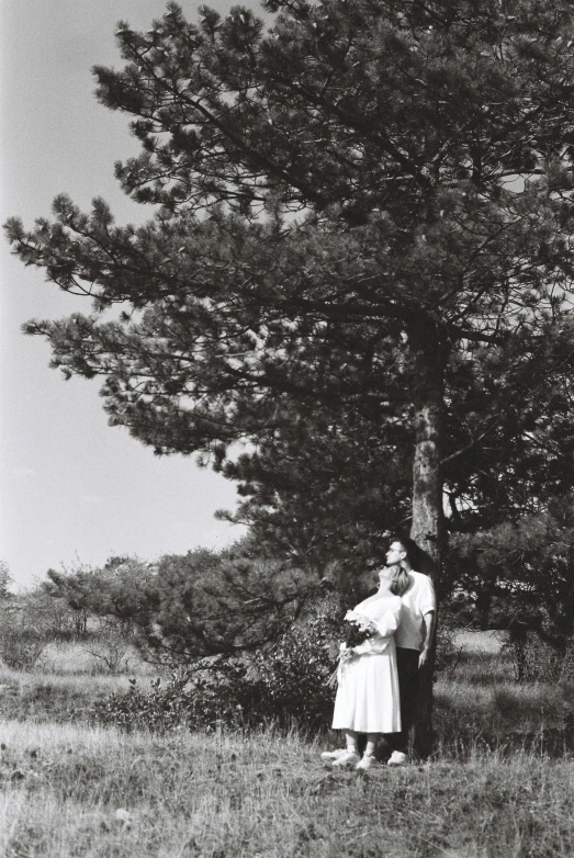 black and white pograph of two people standing in the grass under a large tree