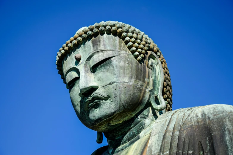 a large buddha statue with eyes closed with a clear sky in the background