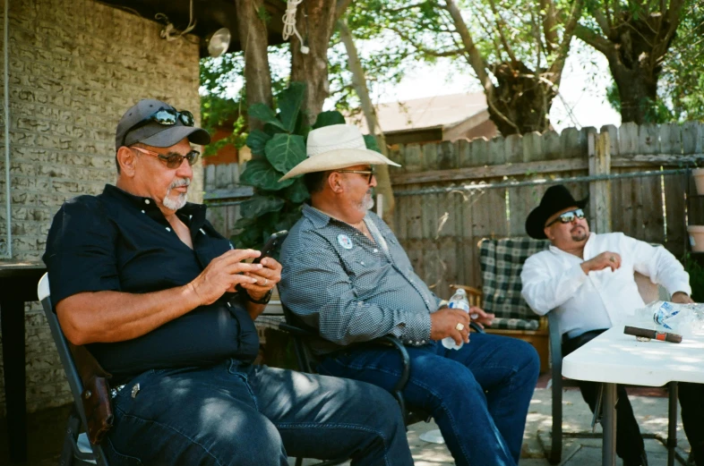 three men sit down in chairs outside on a patio