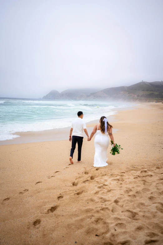 a newly married couple walking on a beach towards the ocean